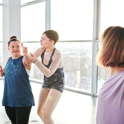 young-yoga-fitness-trainer-activewear-standing-by-disable-girl-helping-her-with-one-exercises-during-physical-training-gym_274679-12034